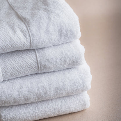 Stack of light gray towels on a beige surface with 'unicot' branding.